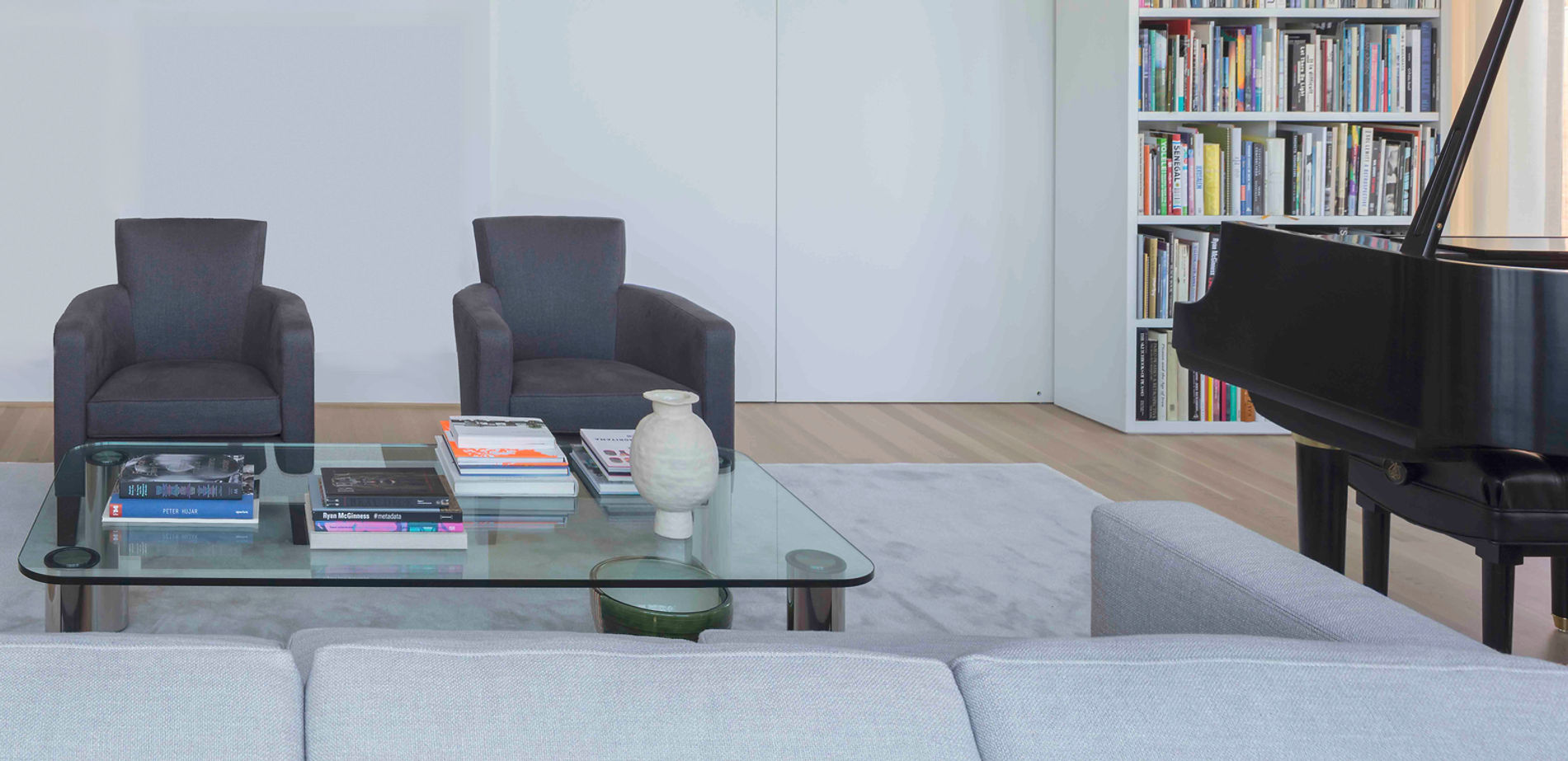 Contemporary living room with dark armchairs, a glass coffee table and a grand piano